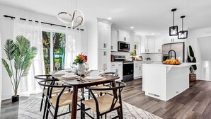 A modern kitchen with white cabinetry, a central island, and a dining area with a round table and chairs.