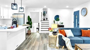 A modern kitchen with white cabinets, a stainless steel refrigerator, and hanging pendant lights.