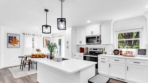 A modern kitchen with white cabinets, a central island, stainless steel appliances, and pendant lighting.