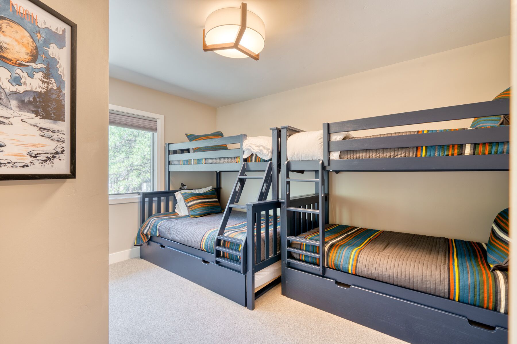 A room with three bunk beds, a window with blinds, a framed picture on the wall, and a ceiling light fixture.