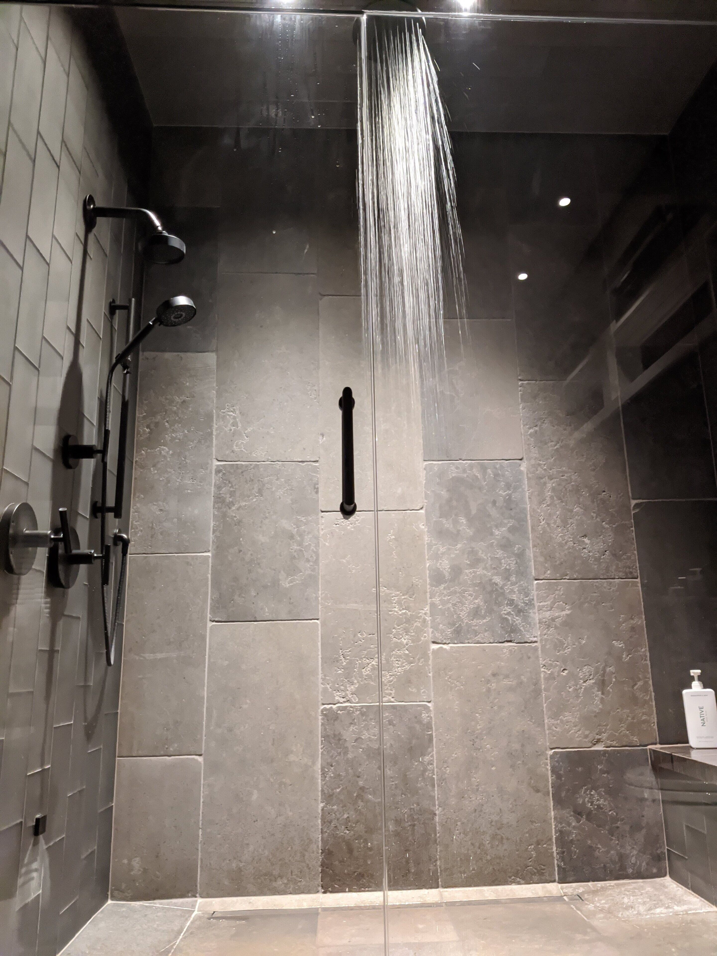 A modern shower with multiple heads and a glass partition.