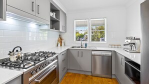 A modern kitchen with white tiles, stainless steel appliances, and a wooden floor. - Driftwood Mudjimba-Beach Holiday (Sunshine Coast)