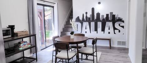 A modern dining area with a round table, chairs, and a cityscape mural on the wall.