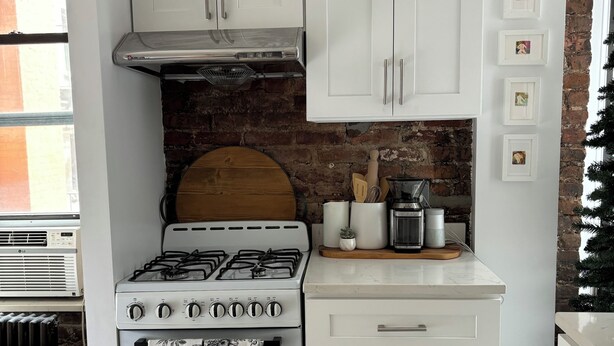Een keuken met witte kasten, een gasfornuis en een bakstenen muur.