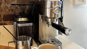 Een koffieapparaat met een koffiekop op een houten tafel, een metalen kan en een bakstenen muur op de achtergrond.