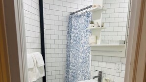 Een badkamer met witte betegelde wanden, een douche met een blauw bloemen gordijn, een wit wastafelmeubel en een toilet.