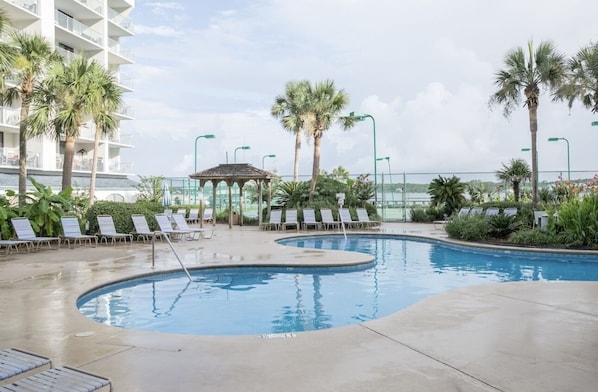A pool area with lounge chairs, palm trees, and a gazebo.