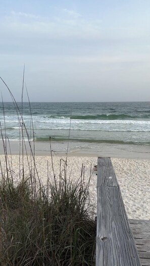 A wooden boardwalk leading to a sandy beach with ocean waves in the background.