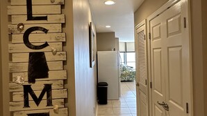 A hallway with a 'WELCOME' sign made of wooden planks and letters, leading to a door with a window.