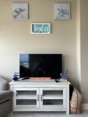 A living room with a flat-screen TV on a wooden cabinet, a wall with three framed artworks, and a motivational sign.
