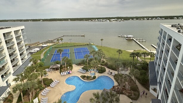 A resort with a swimming pool, tennis courts, and a view of the water.