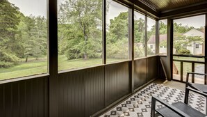 Eine überdachte Veranda mit großen Fenstern, die auf eine grüne Wiese und Bäume blicken.
