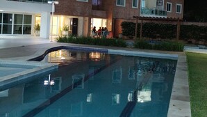 Una piscina con suelo de baldosas, rodeada por un edificio con varios balcones y ventanas.