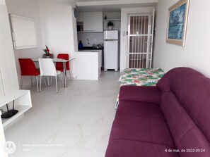 Um espaço compacto com um sofá roxo, área de refeições com cadeiras vermelhas, cozinha com armários brancos e uma porta com portão de metal.
