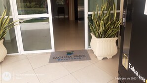 Entrada de un hotel con puerta de vidrio, plantas en macetas, felpudo y un letrero con el nombre del hotel.