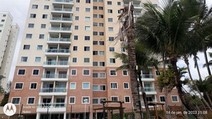 Un edificio residencial de varios pisos con balcones, una palmera y un parque infantil.