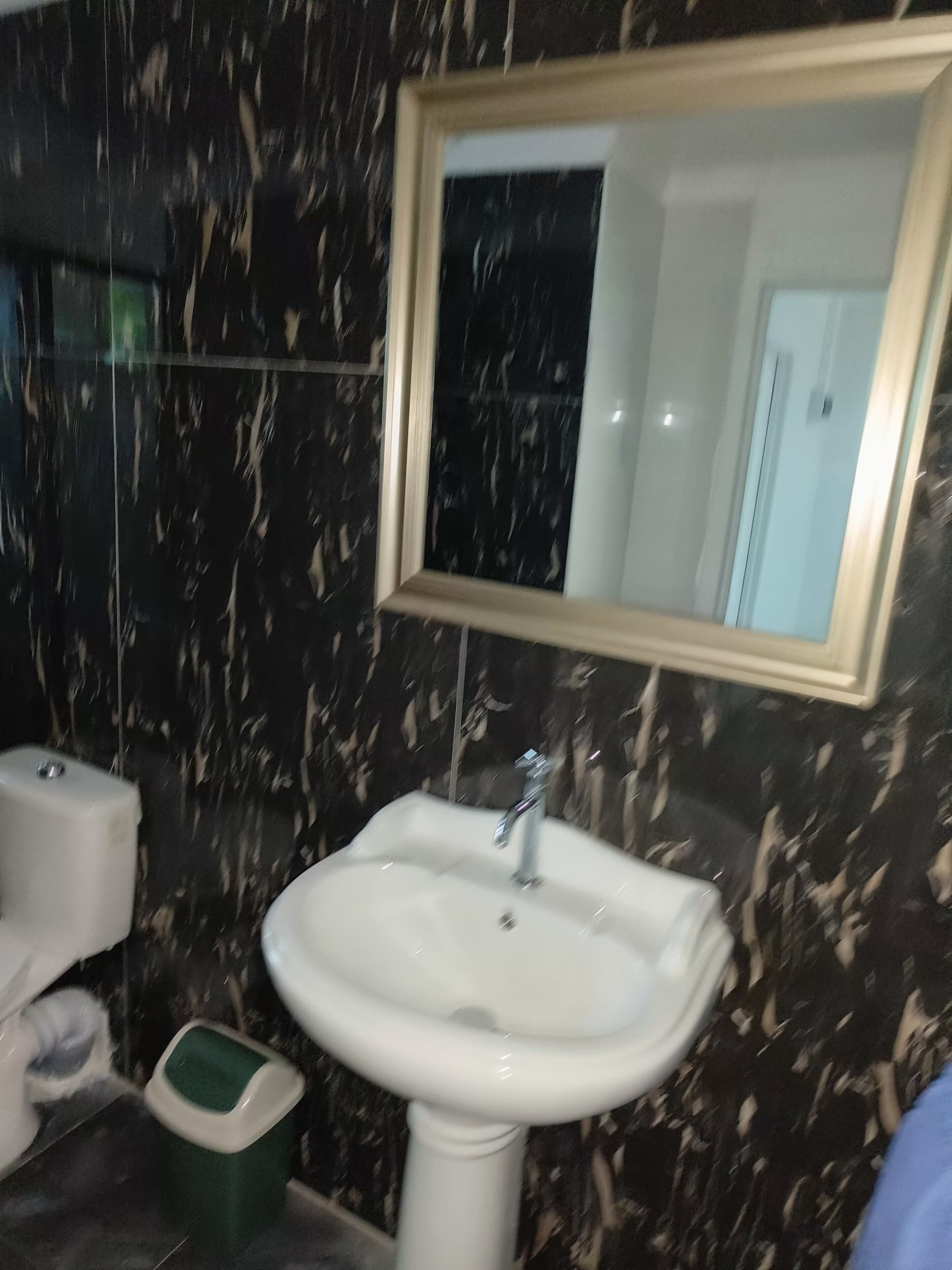 A bathroom with a marble wall, a white sink, and a mirror above it.