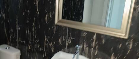 A bathroom with a marble wall, a white sink, and a mirror above it.