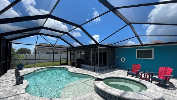 A covered outdoor swimming pool area with a hot tub, lounge chairs, and a view of the backyard. - Sunset Serenity Retreat: Coastal Elegance with Poolside Bliss (New Port Richey)