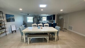 A spacious dining area with a large table and chairs, a kitchen in the background, and a ceiling fan. - Sunset Serenity Retreat: Coastal Elegance with Poolside Bliss (New Port Richey)