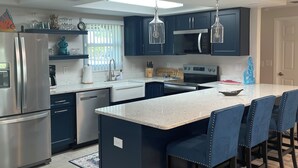 A modern kitchen with dark blue cabinets, stainless steel appliances, and a central island with bar stools. - Sunset Serenity Retreat: Coastal Elegance with Poolside Bliss (New Port Richey)