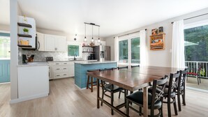A modern kitchen with white cabinets, a blue island, and a dining area with a wooden table and chairs. - Wind Swept Pines
Newly renovated, close to water 3 bedroom cottage (Wiarton)