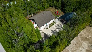 An aerial view of a property with a large building, a covered outdoor area with red chairs, and dense surrounding trees. - Wind Swept Pines
Newly renovated, close to water 3 bedroom cottage (Wiarton)