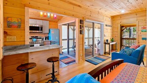 Interior de una cabaña de madera con cocina, comedor y una zona de estar acogedora.