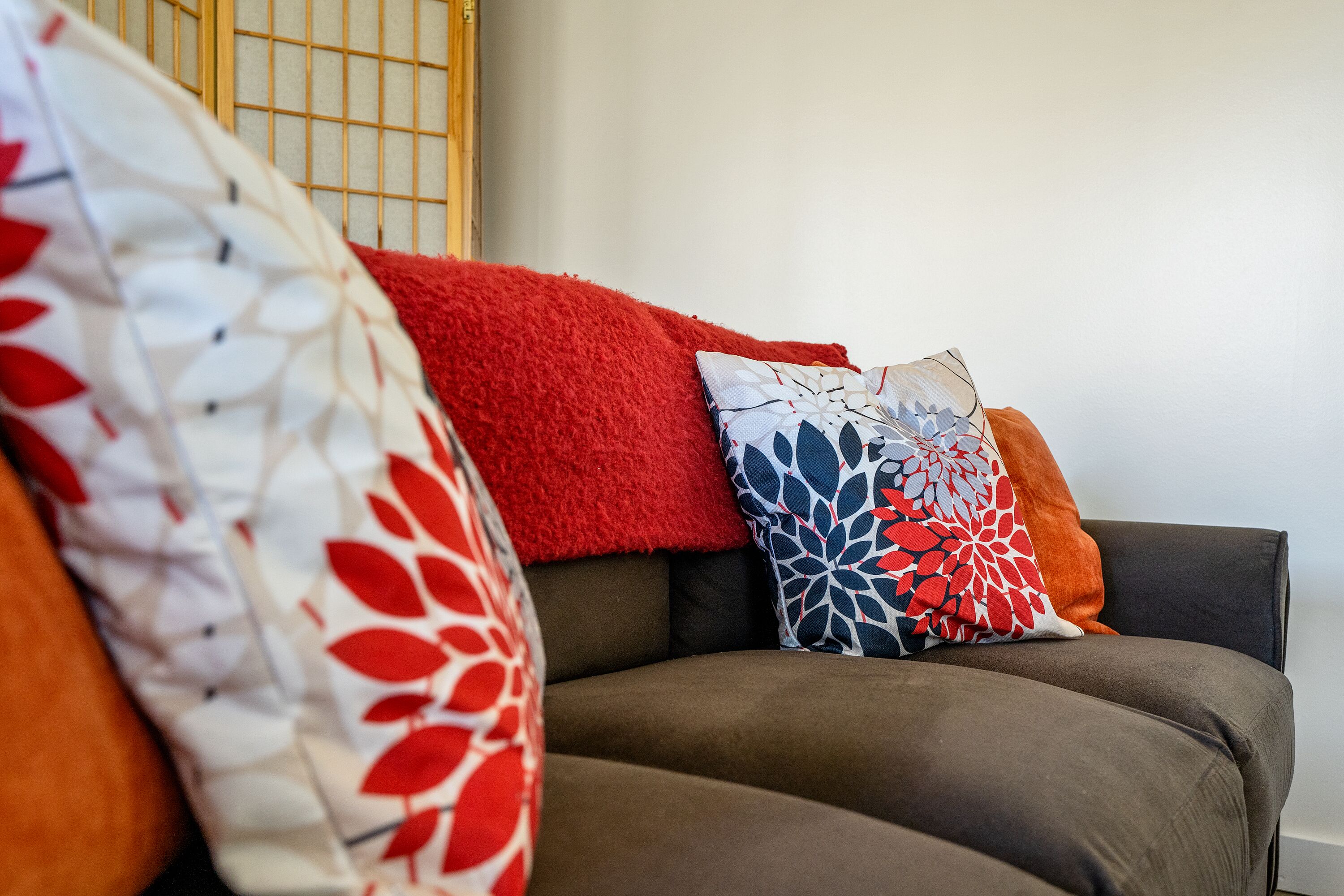 Un sofá con varias almohadas, una manta roja y un cojín estampado.