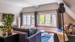 Un dormitorio tipo loft moderno con un ventanal grande, un sofá, una mesita pequeña y una lámpara de pie.