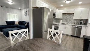 Eine moderne Küche mit weißen Schränken, Edelstahlgeräten und einem Essbereich mit Holztisch und weißen Stühlen.