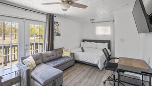 Ein Zimmer mit Deckenventilator, einem Bett, einer Couch, einem Schreibtisch und einem fenster mit Vorhängen.