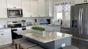 A modern kitchen with white cabinets, stainless steel appliances, a marble countertop, and a central island with bar stools.