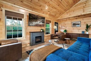 L’intérieur d’une cabane en rondins, avec une cheminée, des fauteuils en cuir et une grande fenêtre.