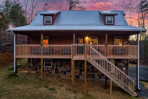 Une cabane en rondins avec des fondations en pierre, un toit en métal et une terrasse en bois dotée d’un escalier.