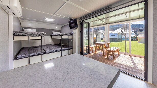 A compact room with bunk beds, a small table, and a sliding glass door leading to an outdoor area. - Gapyeong Ilekaempingjang (Gapyeong)