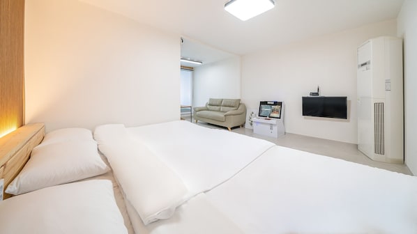 Habitación de hotel con una cama grande, un sofá, un televisor, una nevera pequeña y un armario.