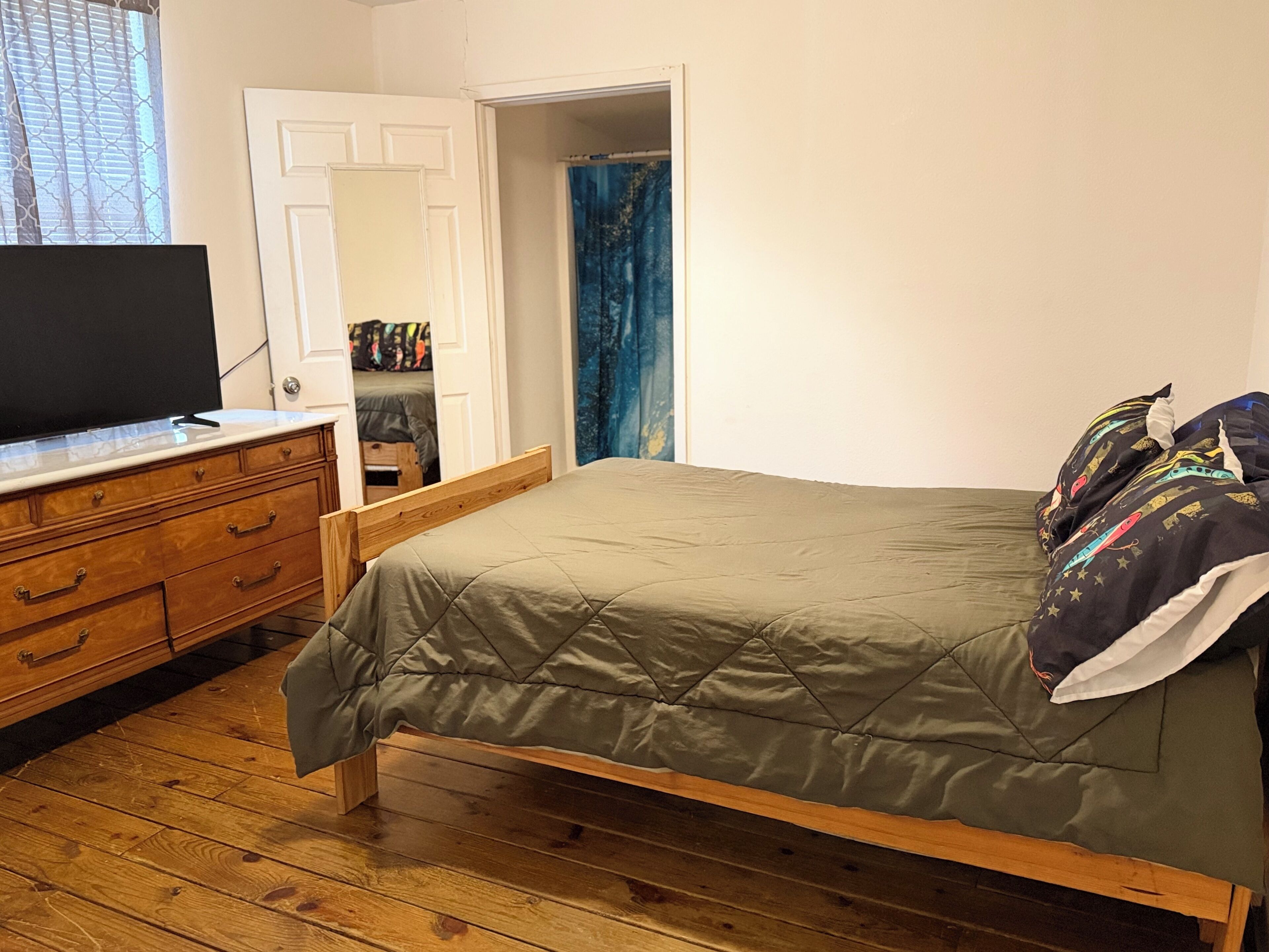 Een slaapkamer met een bed, een houten dressoir en een televisie.