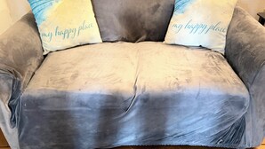 Een grijze bank met twee kussens, waarvan er één de tekst 'my happy place' heeft.