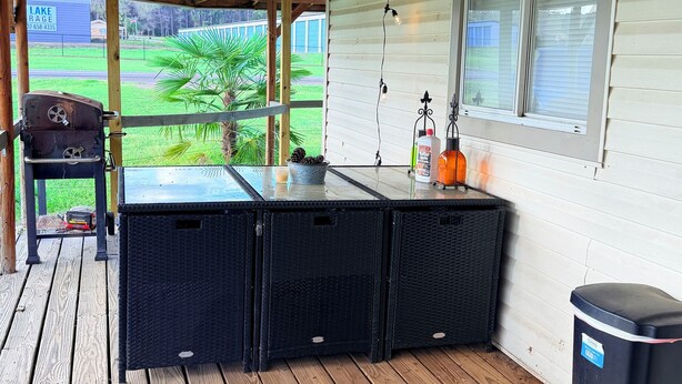 Een overdekt buitengebied met een houten terras, een barbecue en uitzicht op een groen landschap.
