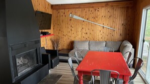 Un salon chaleureux avec une cheminée, une table rouge et un canapé gris.