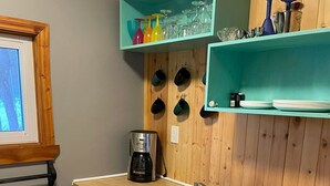 Une cuisine avec un plan de travail en bois, une machine à café, un évier et des étagères remplies de tasses et de verres.