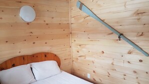 Une pièce de cabane en bois comprenant un lit, une lampe fixée au mur et une batte de bois accrochée au mur.