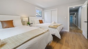 Une chambre d’hôtel avec trois lits, un lustre, une fenêtre et un couloir.