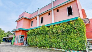 A pink building with a green roof and a hedge in front. - Spot On 91376 Hotel Bintang Flores (Cilacap)