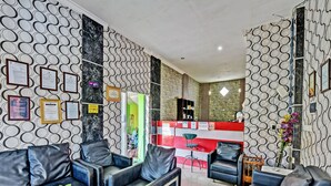 A modern living room with leather sofas, a coffee table, and a reception desk with a red and white color scheme. - Spot On 91376 Hotel Bintang Flores (Cilacap)