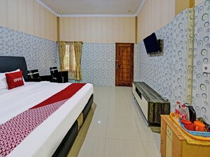 Ein Hotelzimmer mit einem Bett, einer Holzbank, einem an der Wand montierten Fernseher und einem kleinen Tisch mit Toilettenartikeln.