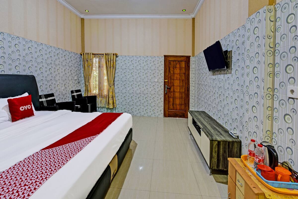 Habitación de hotel con cama, un banco de madera, televisión montada en la pared y una mesita con artículos de aseo.