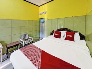 Habitación de hotel con una cama grande, dos almohadas rojas con el logo 'OYO' y una silla de madera, además de paredes con azulejos verdes.