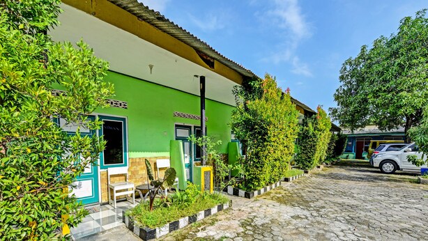 A green building with a cobblestone courtyard, white chairs, and a parked car. - Spot On 91376 Hotel Bintang Flores (Cilacap)